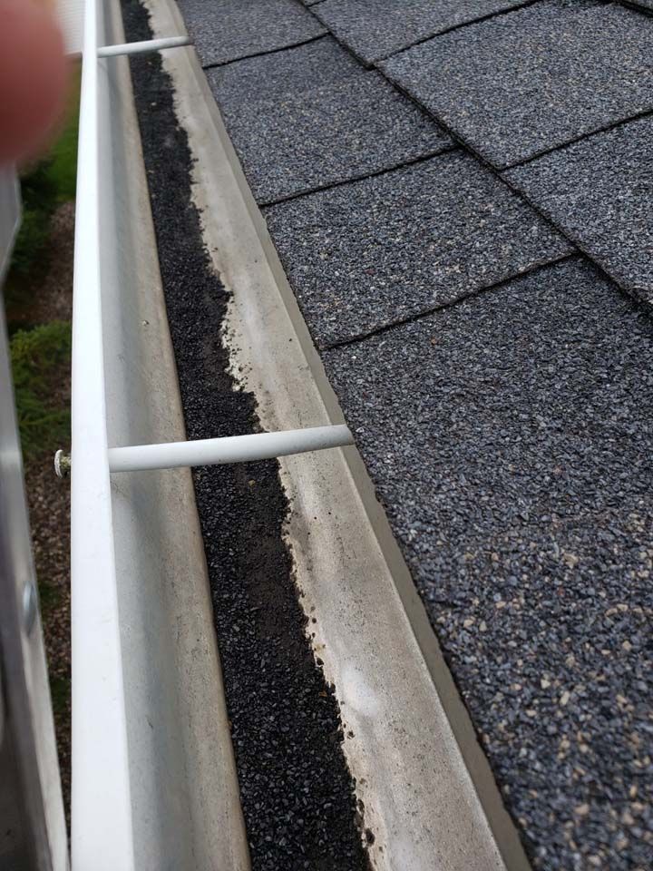 A close up of a gutter on a roof with shingles.