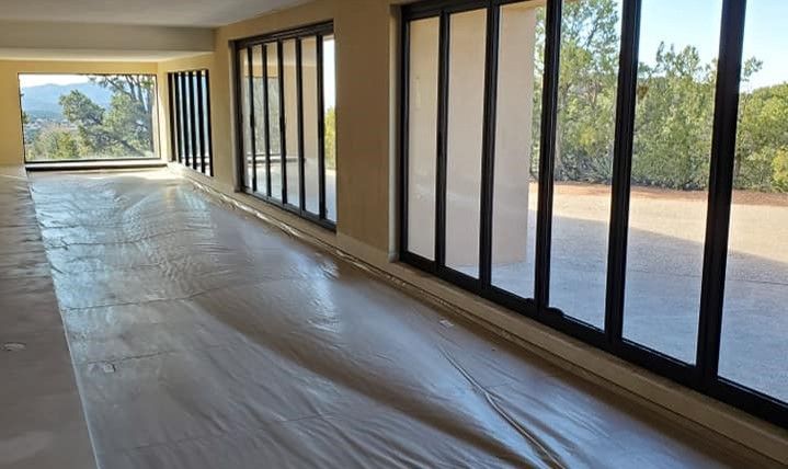 An empty room with a lot of windows and a plastic sheet on the floor.