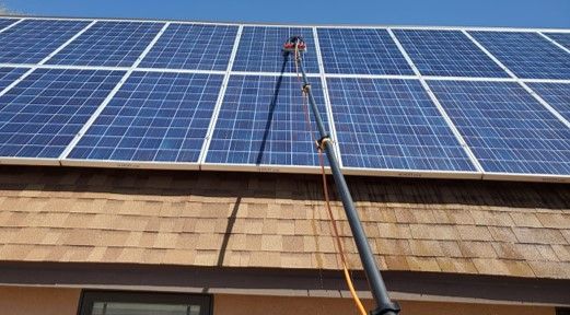 A person is cleaning solar panels on the roof of a building.