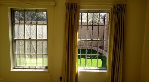 A room with two windows with bars on them and curtains.