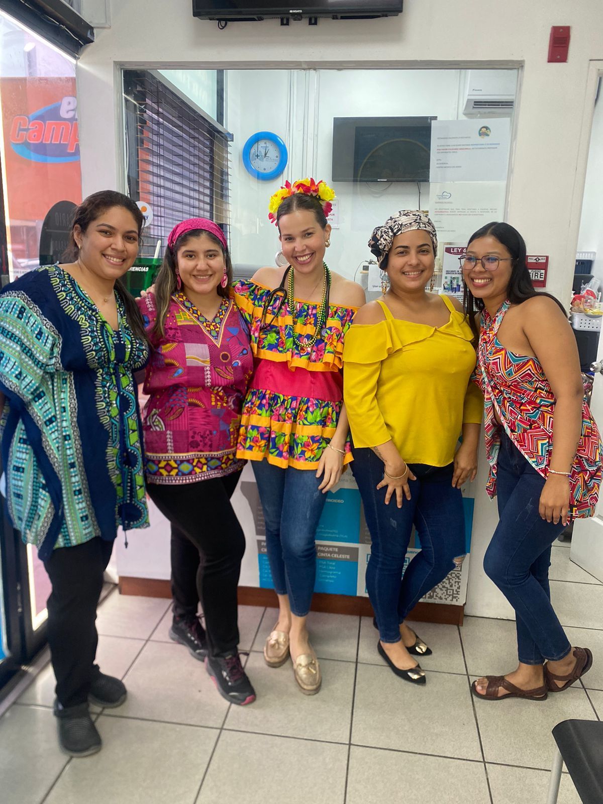 Cinco mujeres con trajes coloridos posan dentro de una oficina bien iluminada.