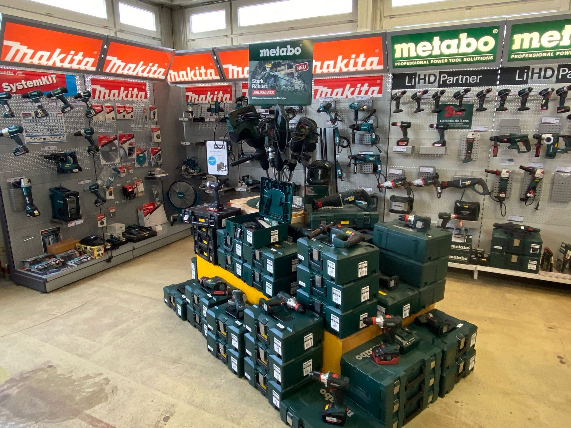 Un présentoir de quincaillerie mettant en vedette les outils électriques Makita et Metabo, avec des étagères et des coffrets à outils empilés.