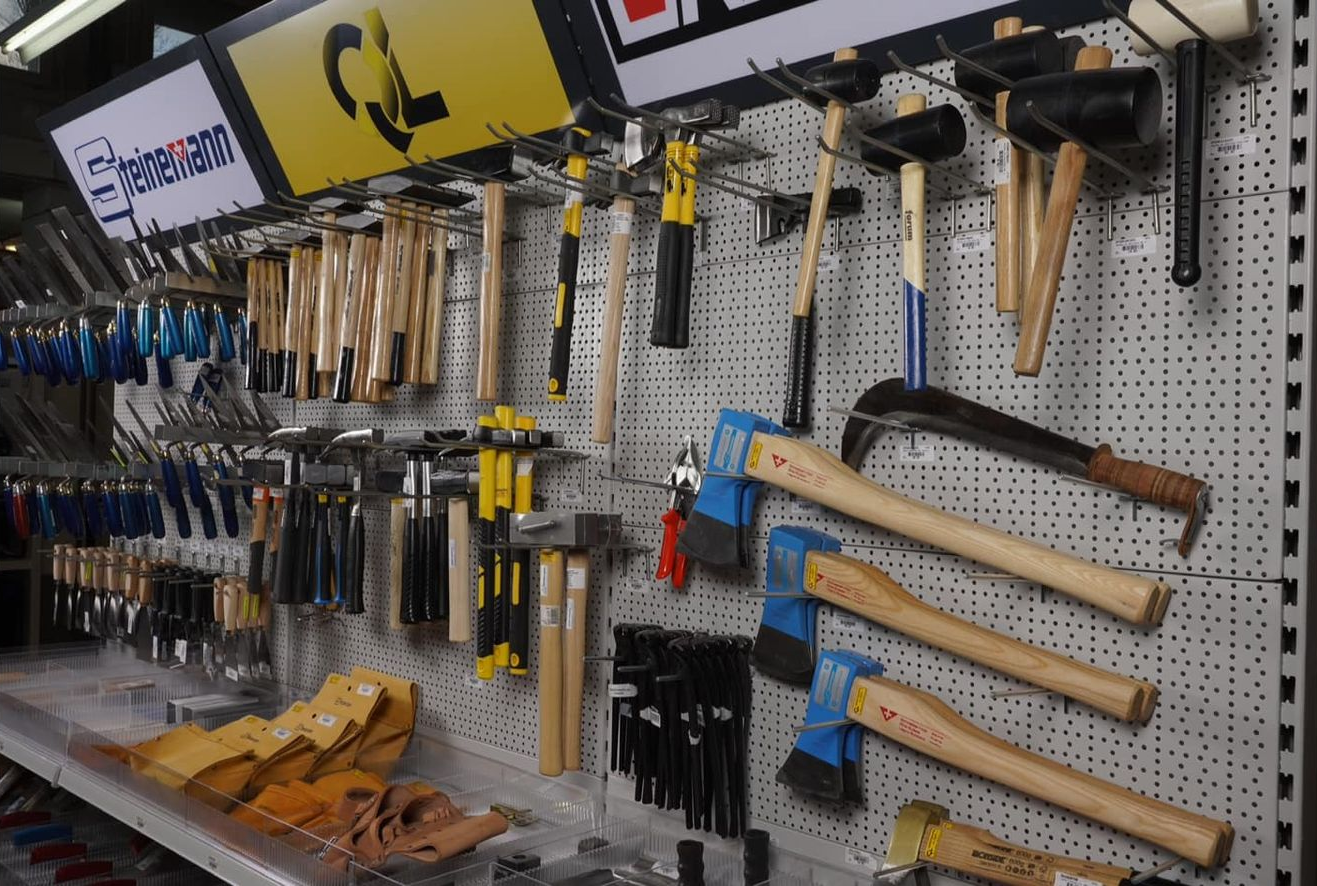 Outils présentés sur un panneau perforé de magasin : marteaux, haches, maillets et autres outils à main.