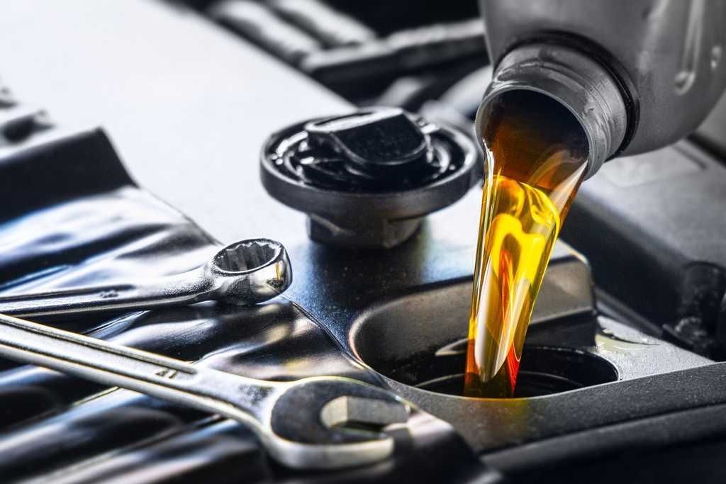 A bottle of oil is being poured into a car engine  | JB Auto CARE