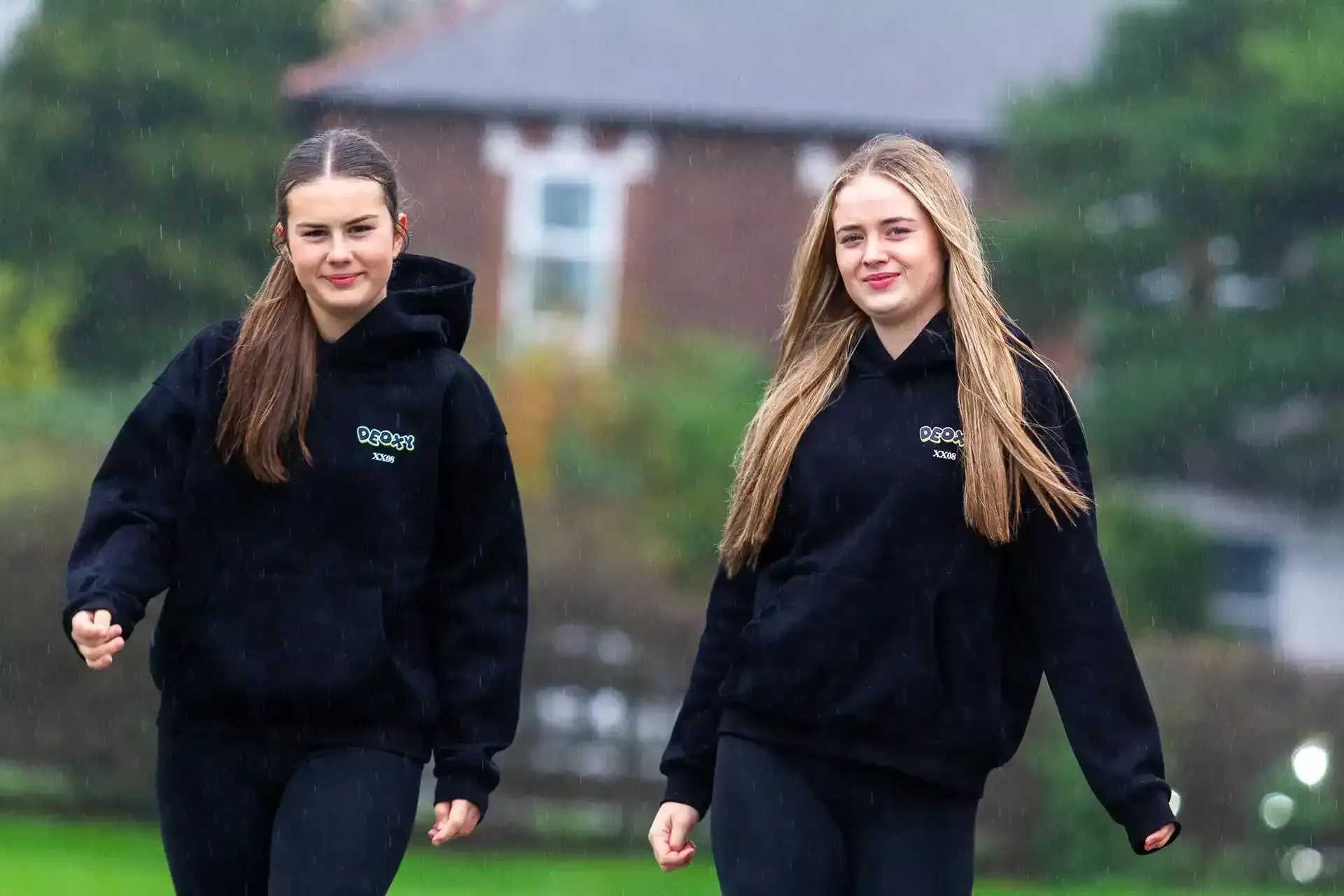 Two girls in black hoodies are walking in a field.