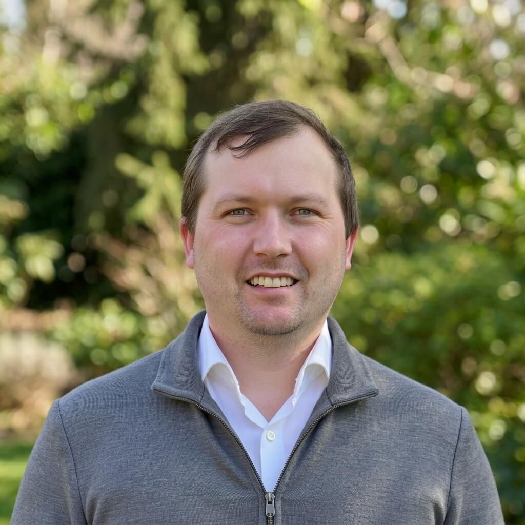 Photo of Jaime in a  one quarter zip pull over in grey with a white shirt in front of a blurred out green background.