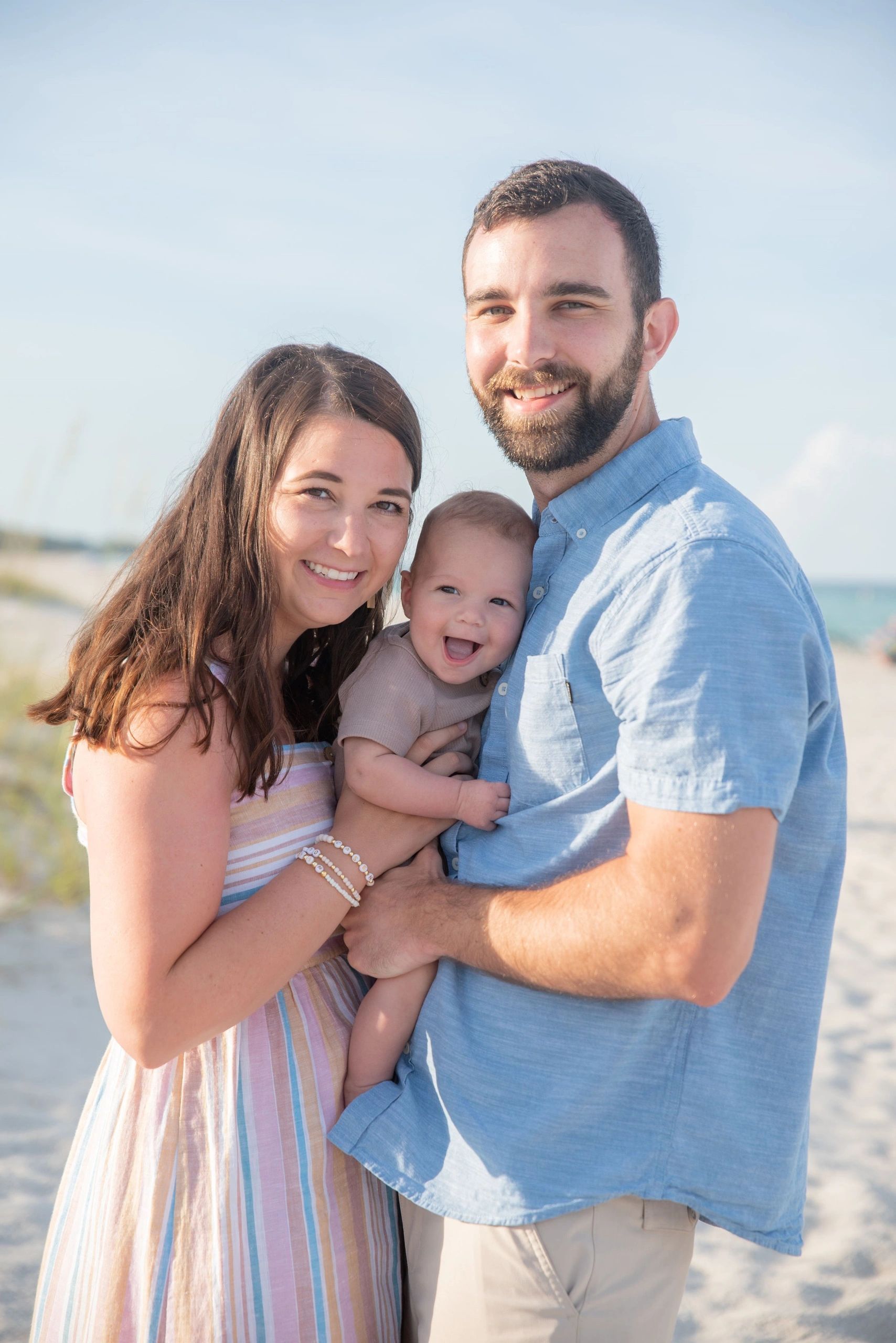 A man and a woman are holding a baby on the beach.