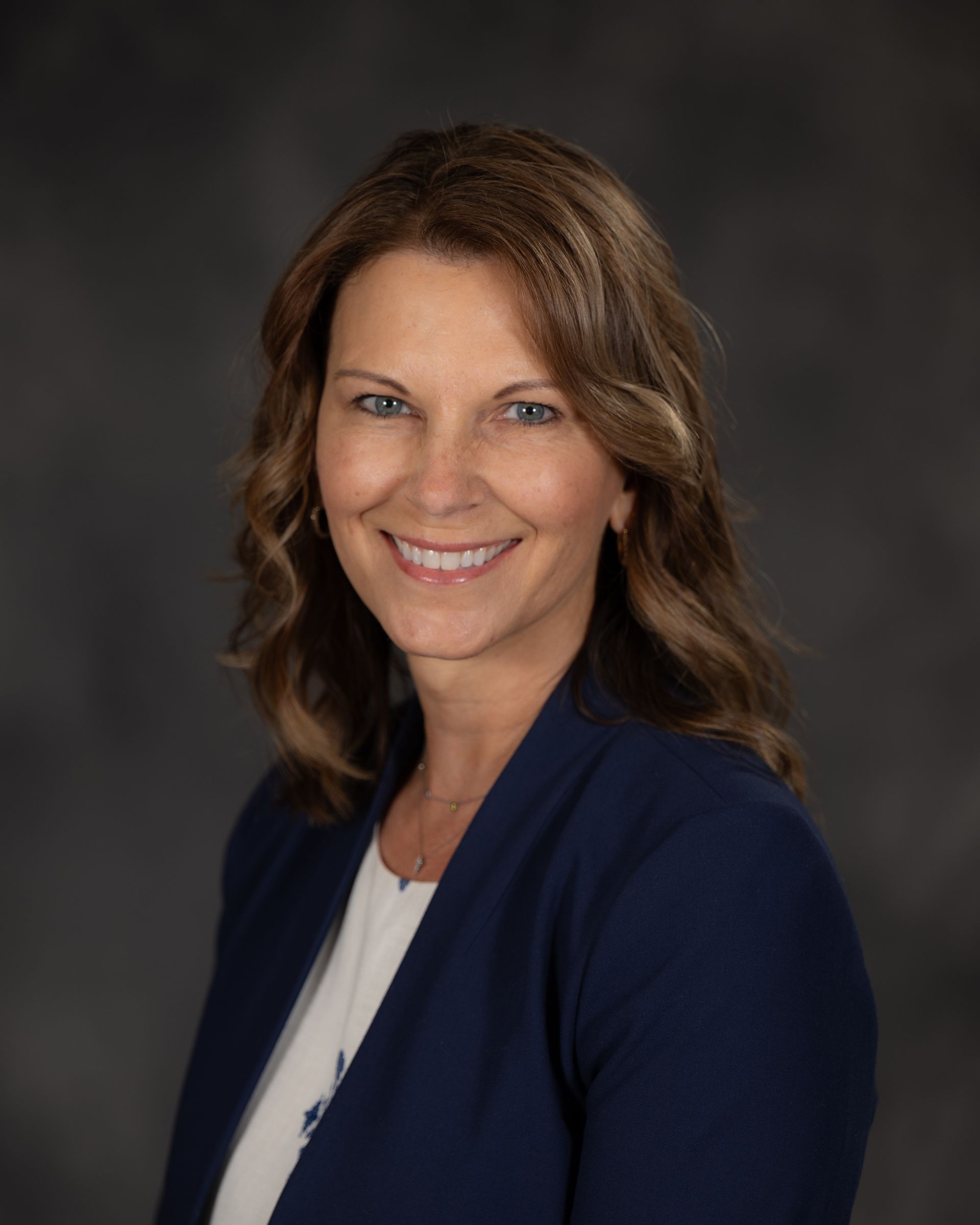 A woman in a green shirt and black jacket is smiling for the camera.