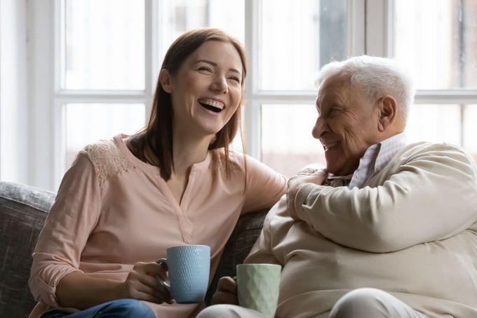 A woman is sitting next to an older man on a couch holding cups of coffee.