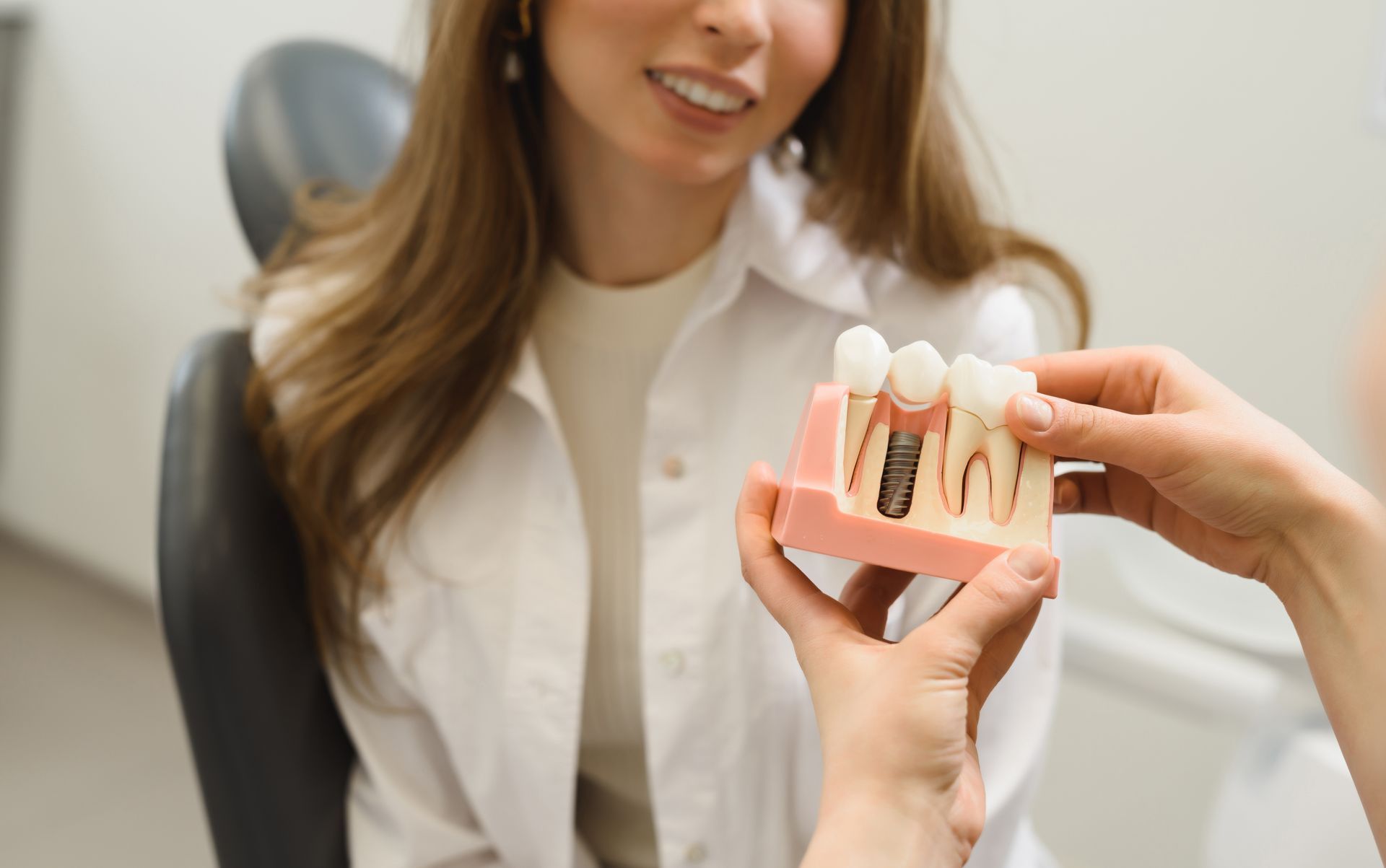 A woman is sitting in a dental chair while a dentist holds a model of her teeth.
