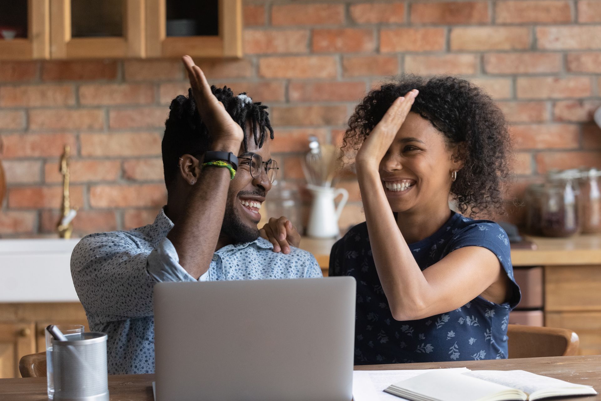 A man and a woman are giving each other a high five while sitting in front of a laptop computer.