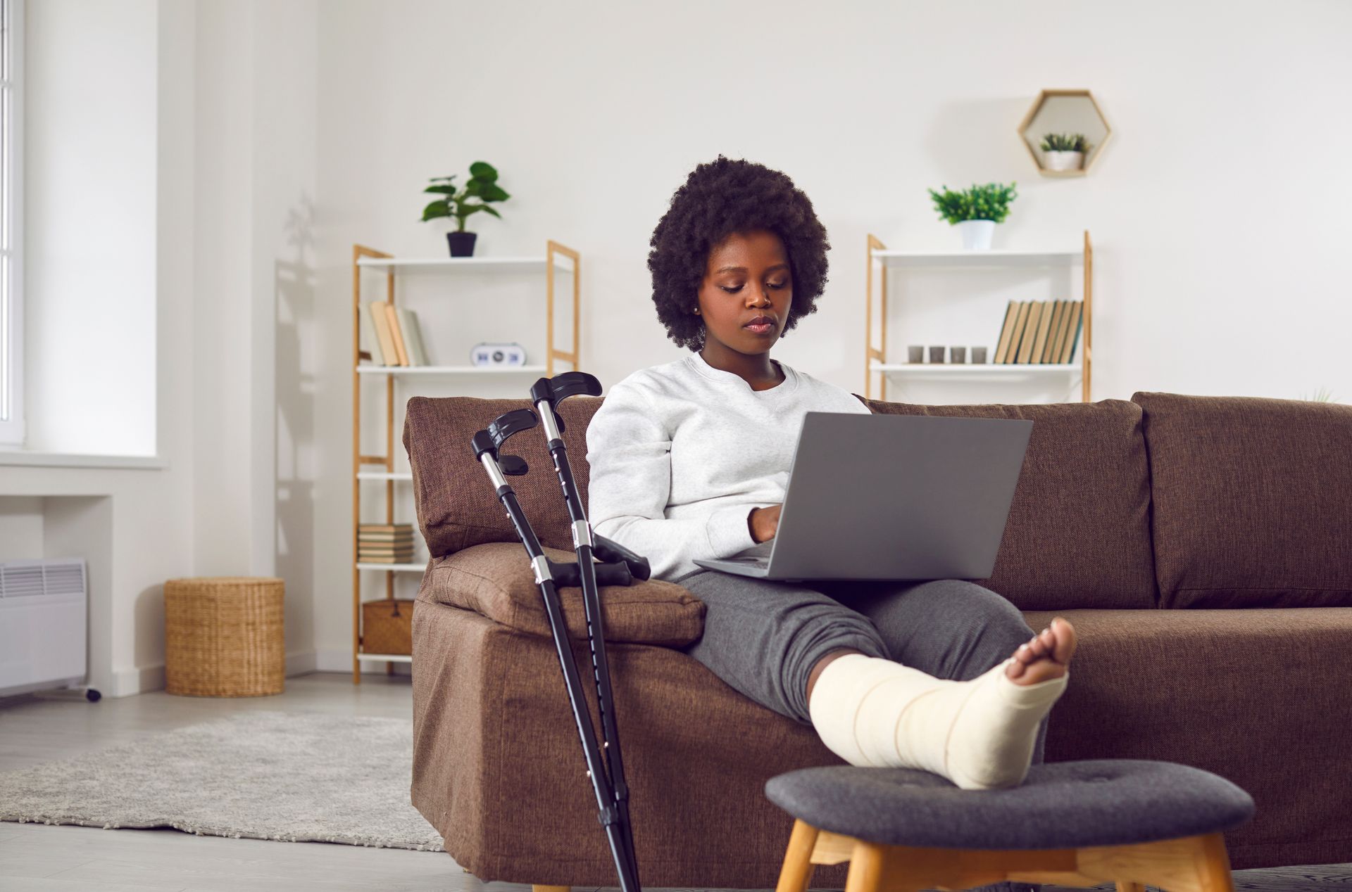 A woman with a cast on her leg is sitting on a couch using a laptop computer.