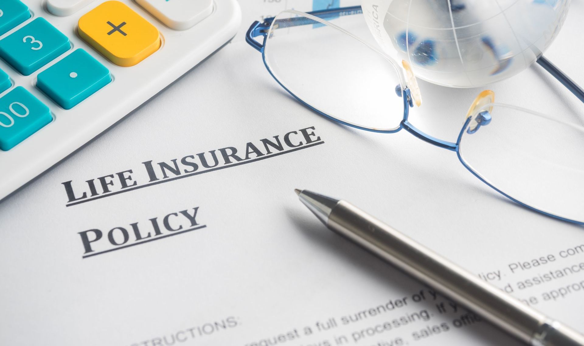 A pen is sitting on top of a life insurance policy next to a calculator and glasses.