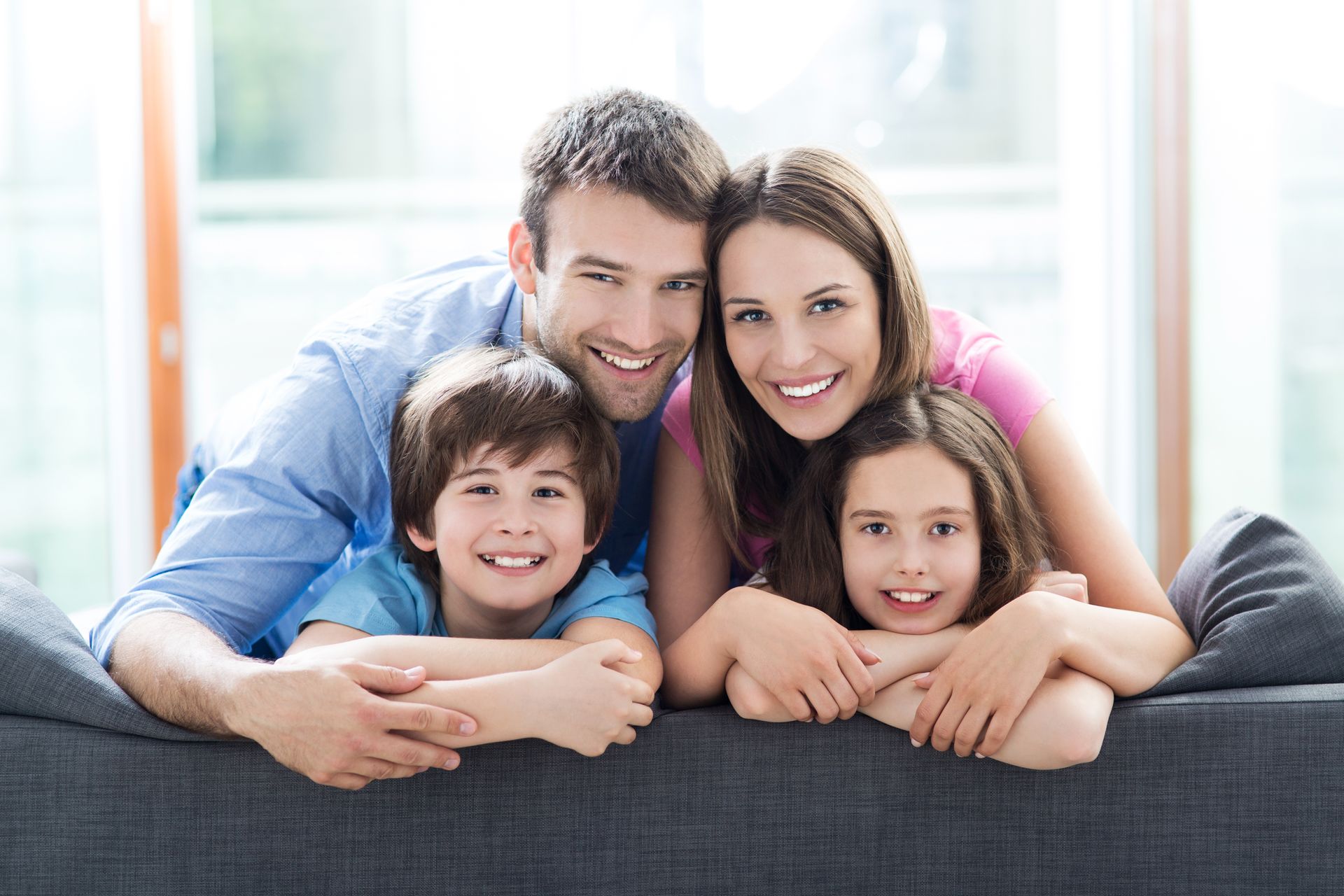A family is laying on a couch and smiling for the camera.
