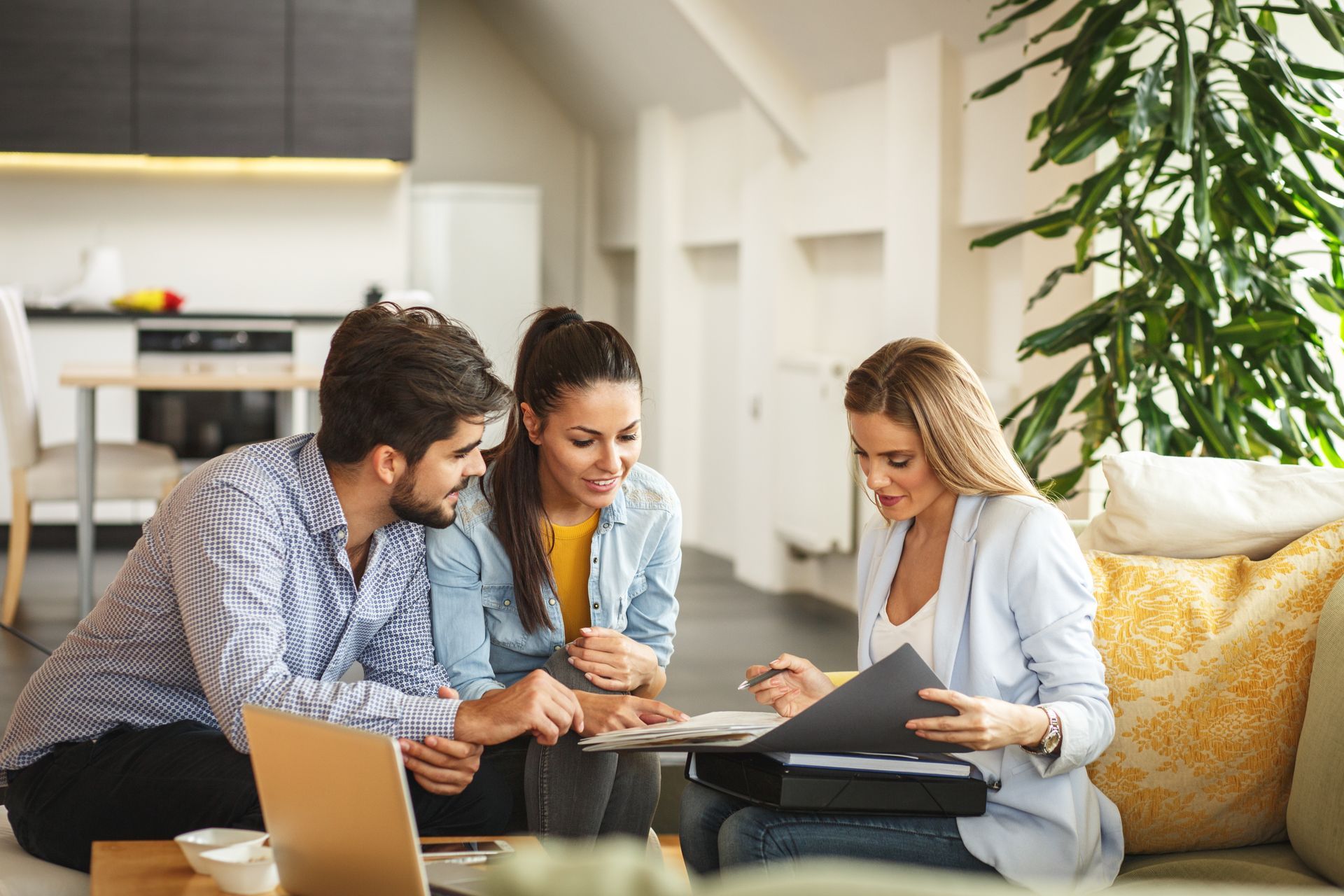 A man and a woman are sitting on a couch talking to a real estate agent.