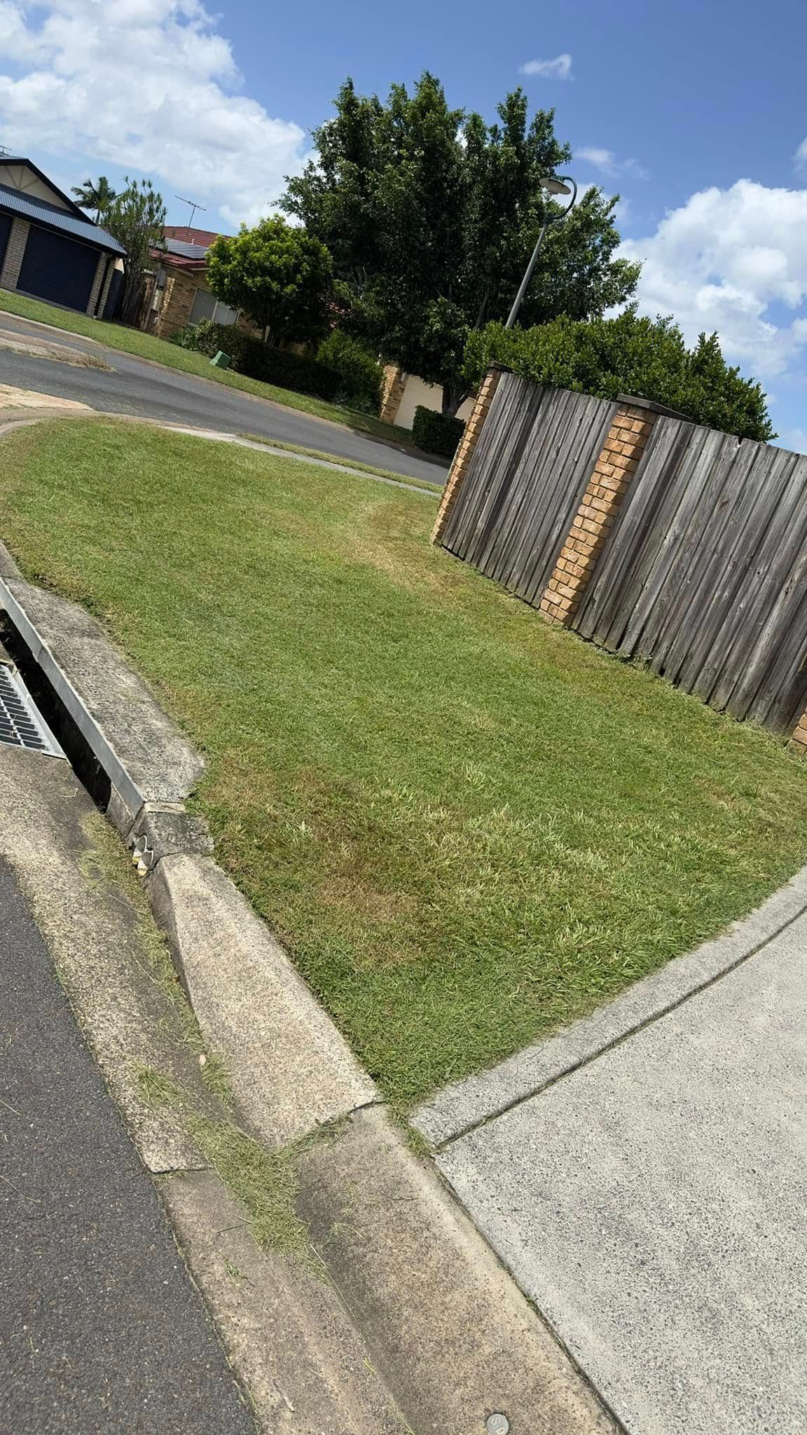 A lawn next to a sidewalk and a fence in a residential area.