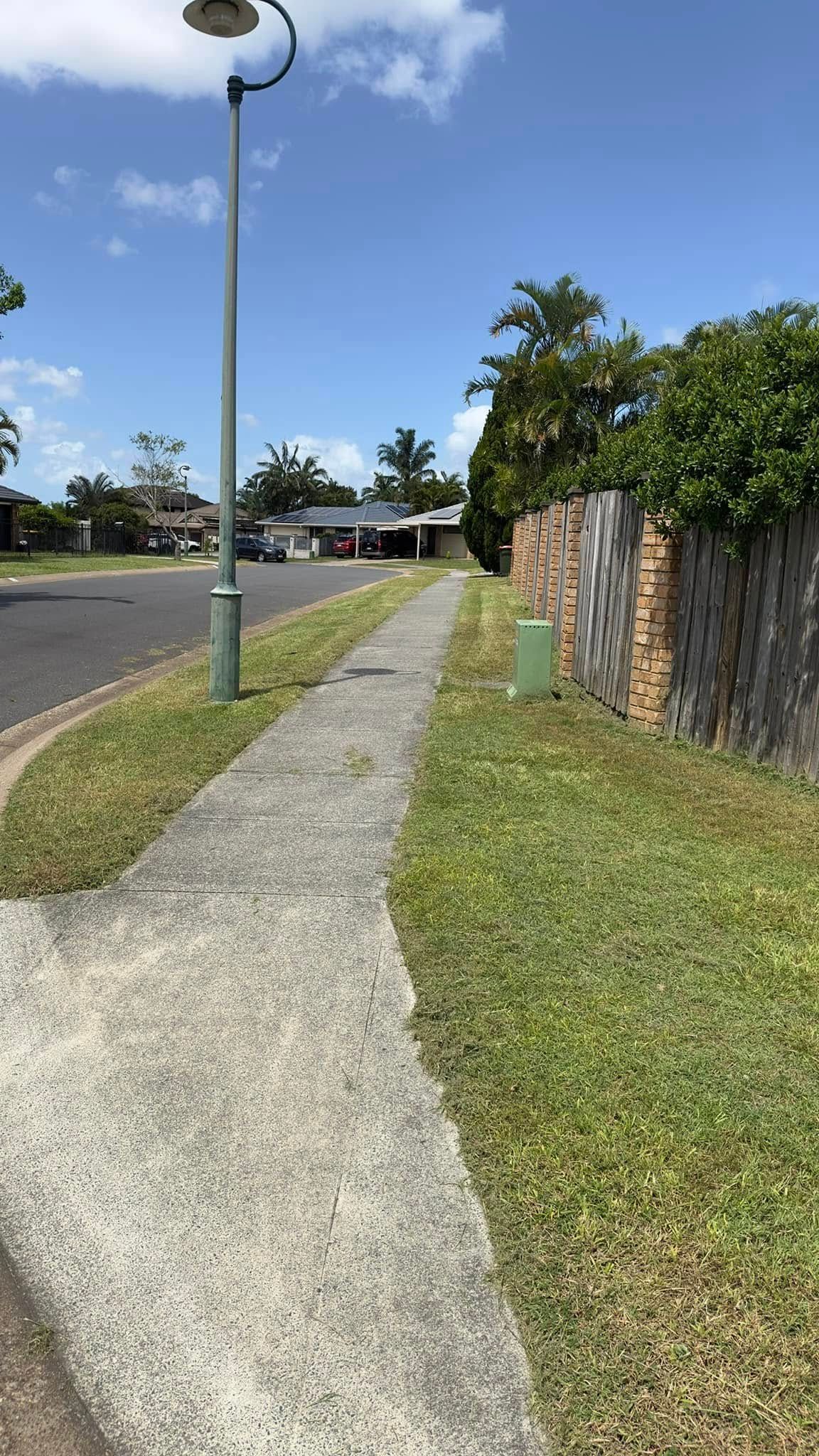 A sidewalk leading to a fence and a house on a sunny day.