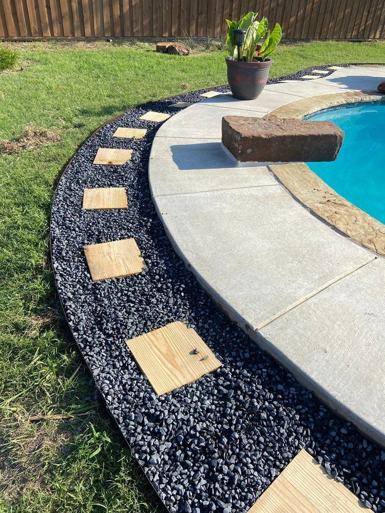 A swimming pool is surrounded by gravel and wooden stepping stones.
