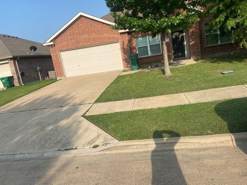 A shadow of a person is cast on the sidewalk in front of a brick house.