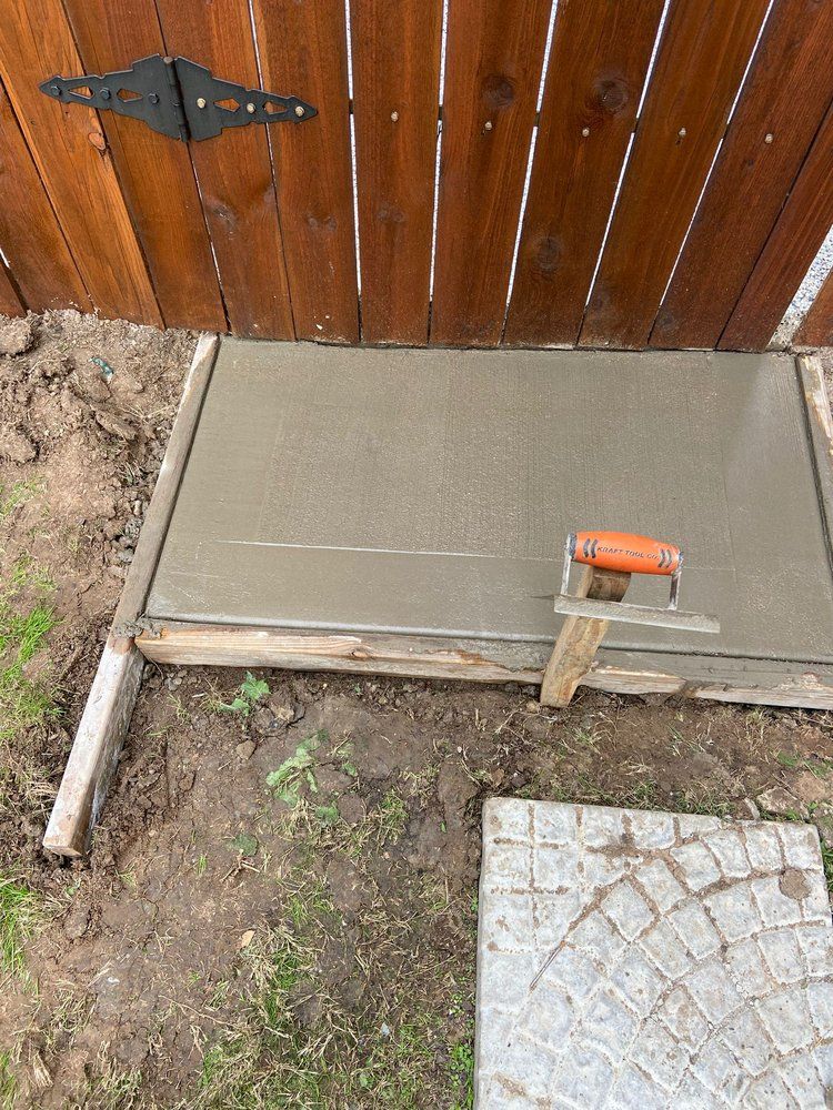 A trowel is sitting on top of a concrete slab next to a wooden fence.
