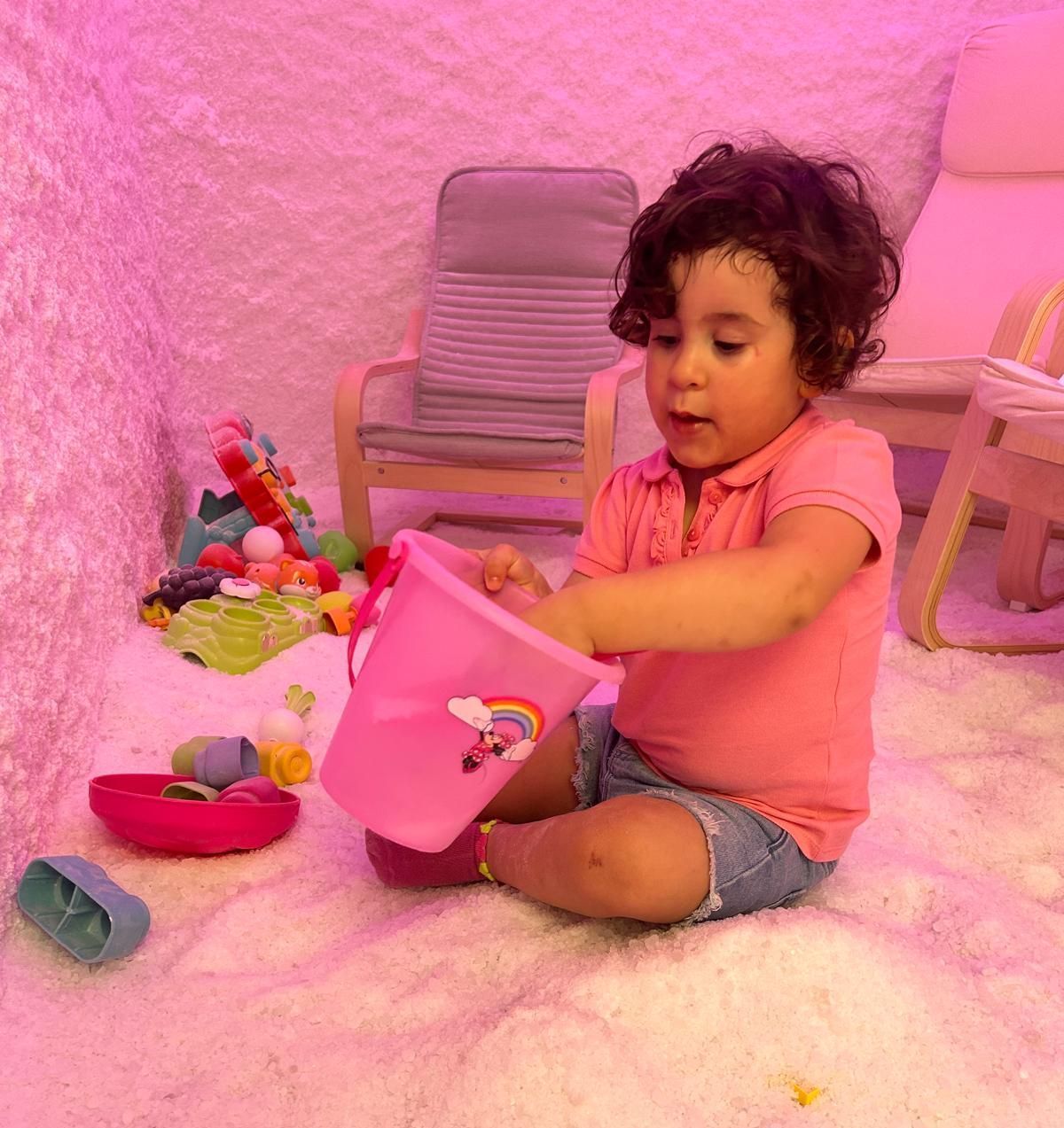 Una bambina è seduta sul pavimento e gioca con un secchiello rosa.