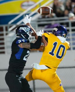 Football players, #10 in yellow and #27 in blue, jumping for ball in stadium.