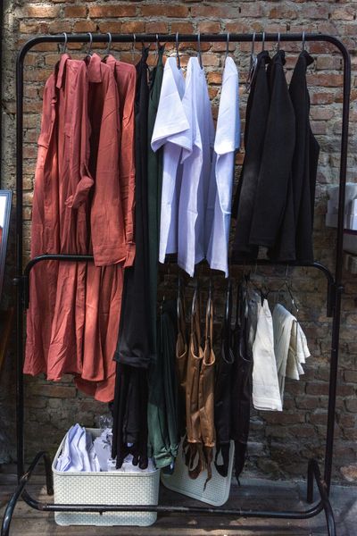 Clothing rack with assorted clothing: rust, white, black, and brown against a brick wall.