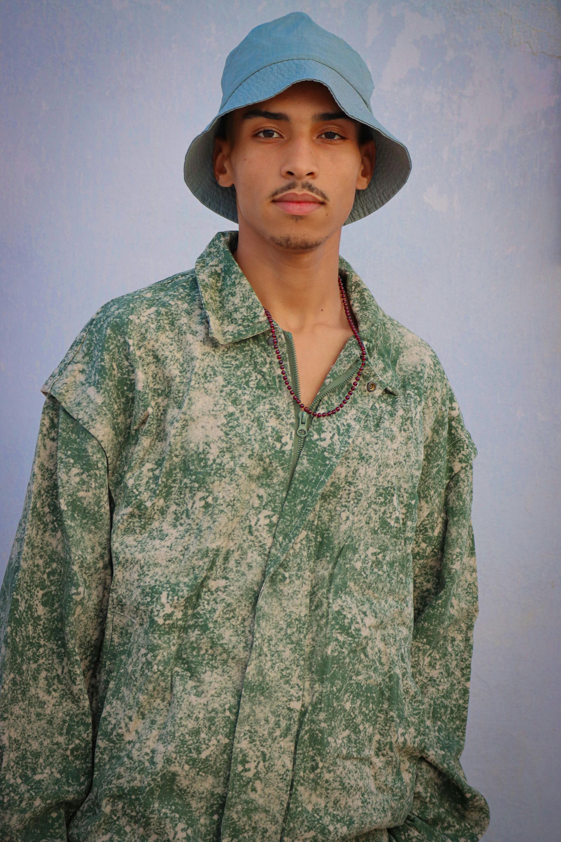 Young person in blue hat and green camouflage jacket, looking at camera.