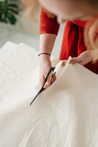 Woman in red dress cutting light fabric with scissors.