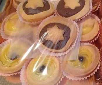 Assortimento di pasticcini in pirottini di carta, alcuni con guarnizione di cioccolato e a forma di stella, altri con ripieno giallo.