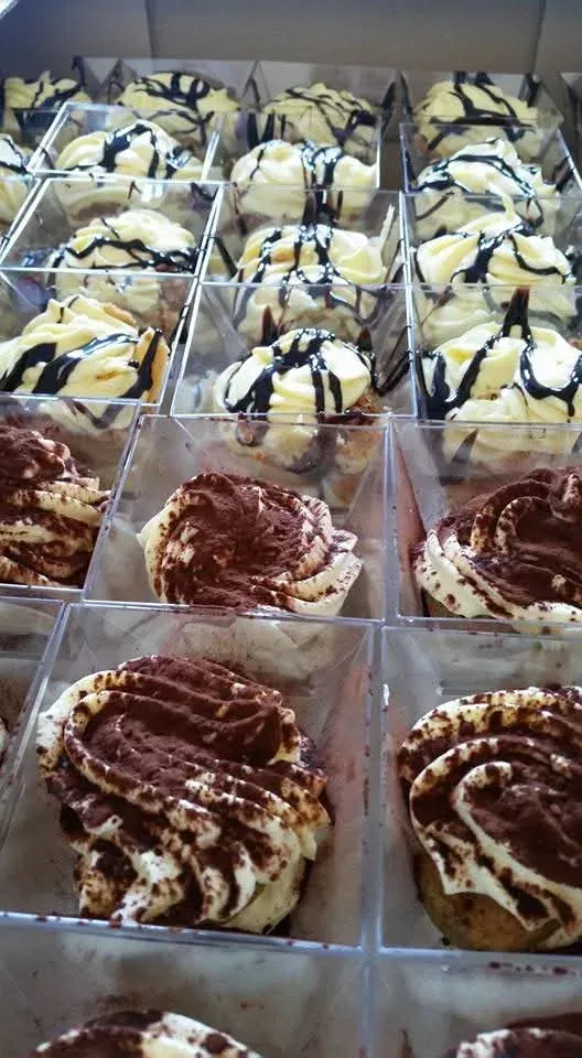 Esposizione di tiramisù e pasticcini alla crema in singole scatole trasparenti, alcuni ricoperti di cioccolato, altri spolverati con cacao in polvere.