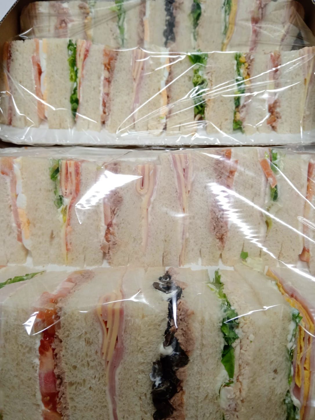 Panini avvolti in pellicola trasparente, impilati in file, con vari ripieni visibili.