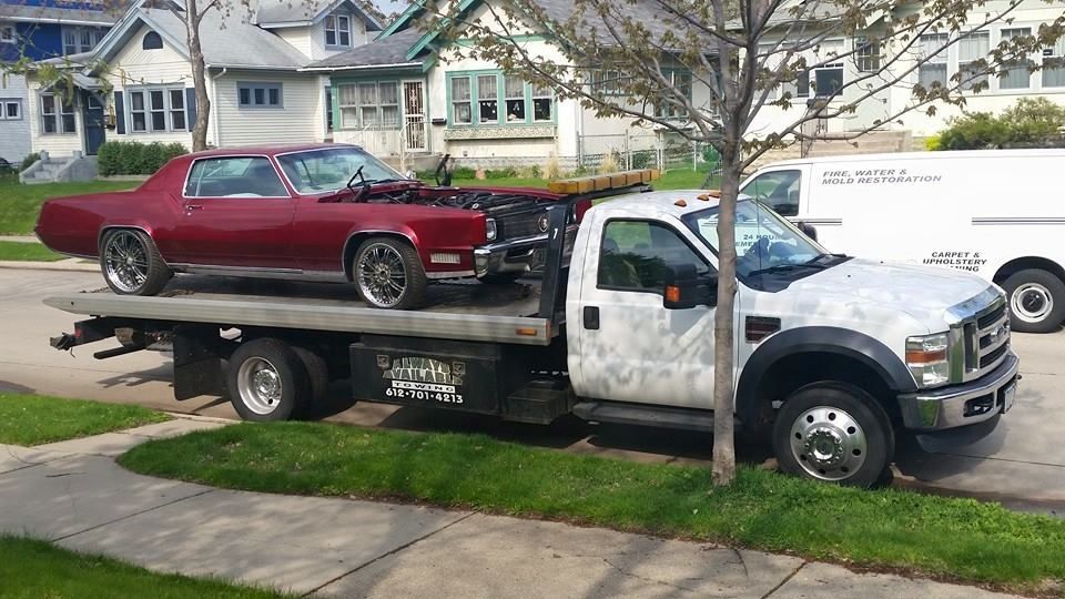 Red classic car on a flatbed tow truck parked on a residential street.