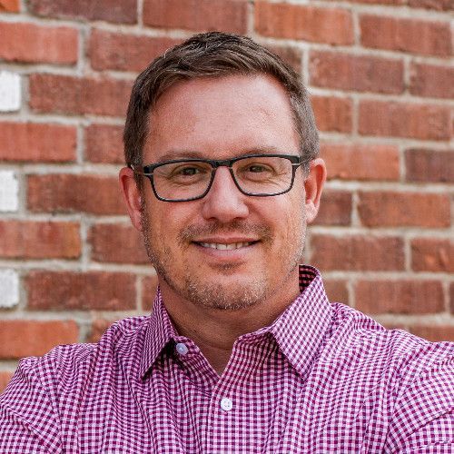 CEO Korey Korfiatis smiling in front of a brick wall.