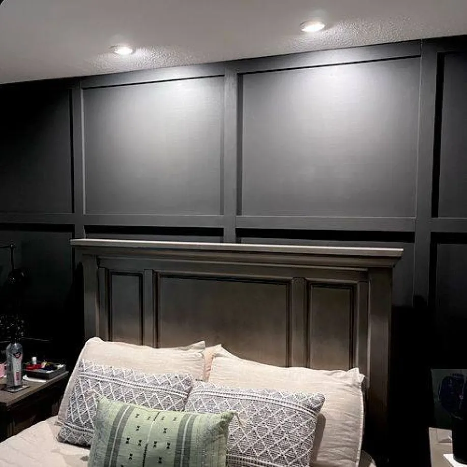 A bedroom with a bed , nightstand , and black wall paneling.