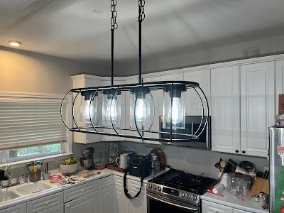 A kitchen with white cabinets , a stove , a sink , and a light fixture hanging from the ceiling.