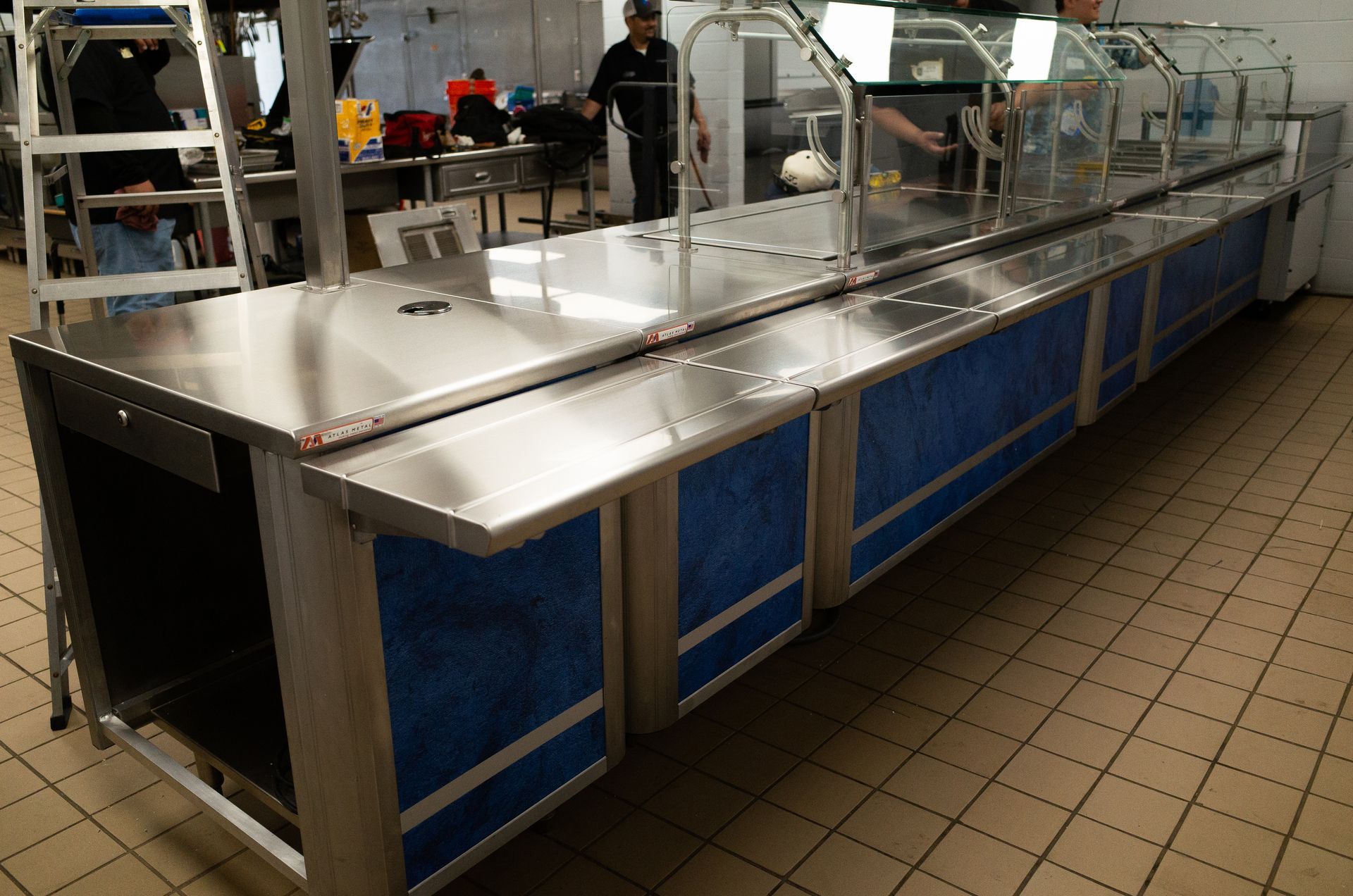 Photo of Integrus Fabrication Team installing a stainless steel and glass kitchen cafeteria serving line