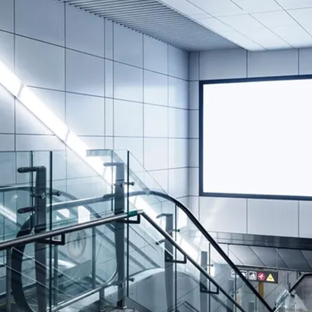A subway station with an escalator and a billboard on the wall.
