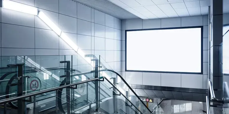 A subway station with an escalator and a billboard on the wall.