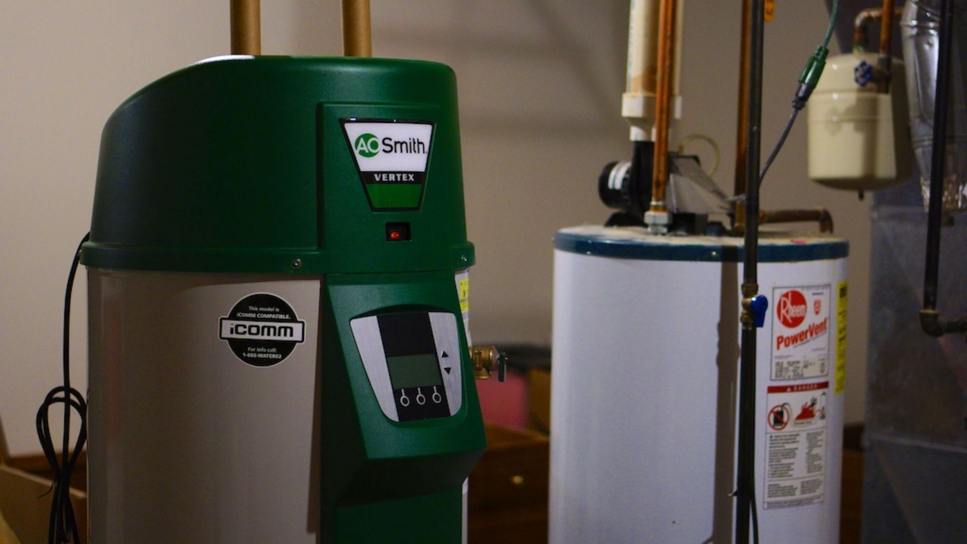 A green water heater is sitting next to a white water heater in a basement.