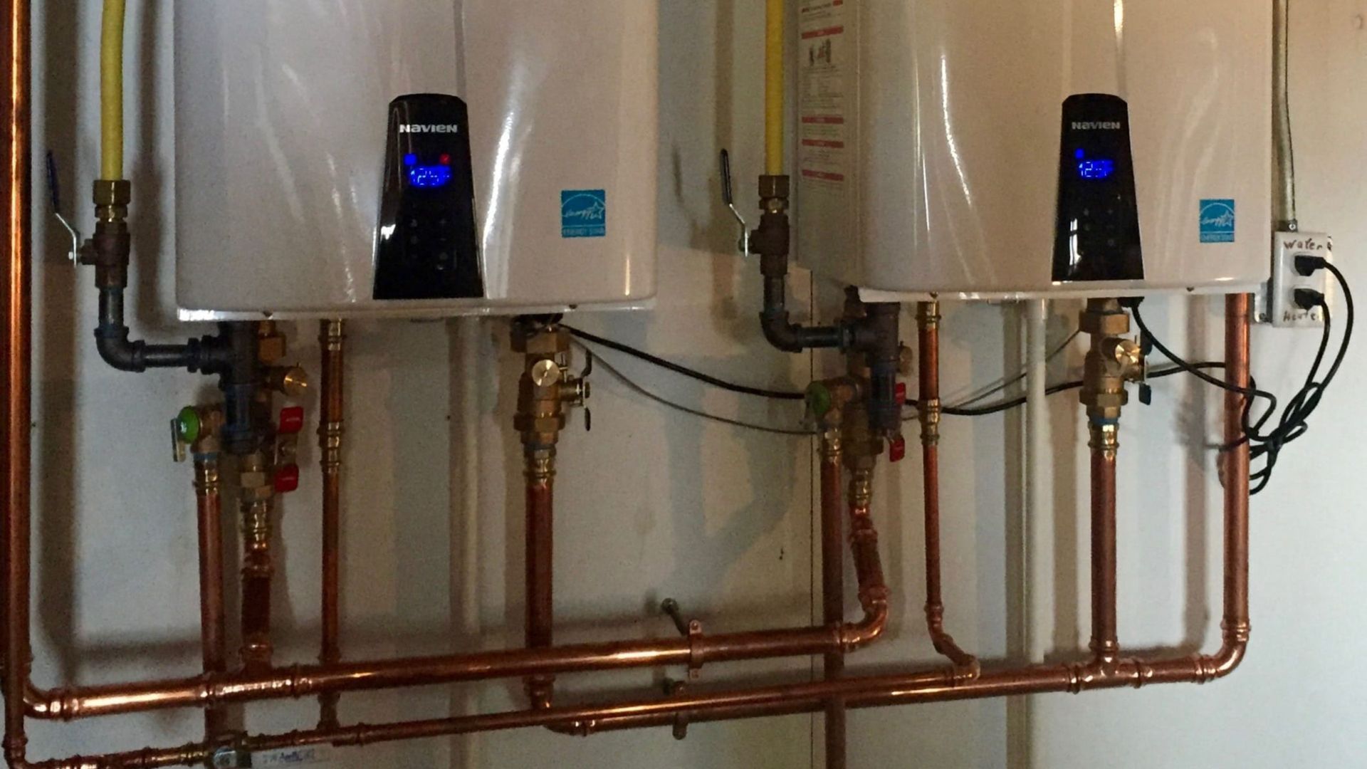 Two water heaters are connected to copper pipes on the wall.