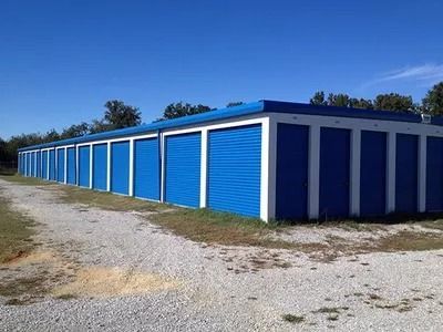 A row of blue and white storage units on a gravel road.