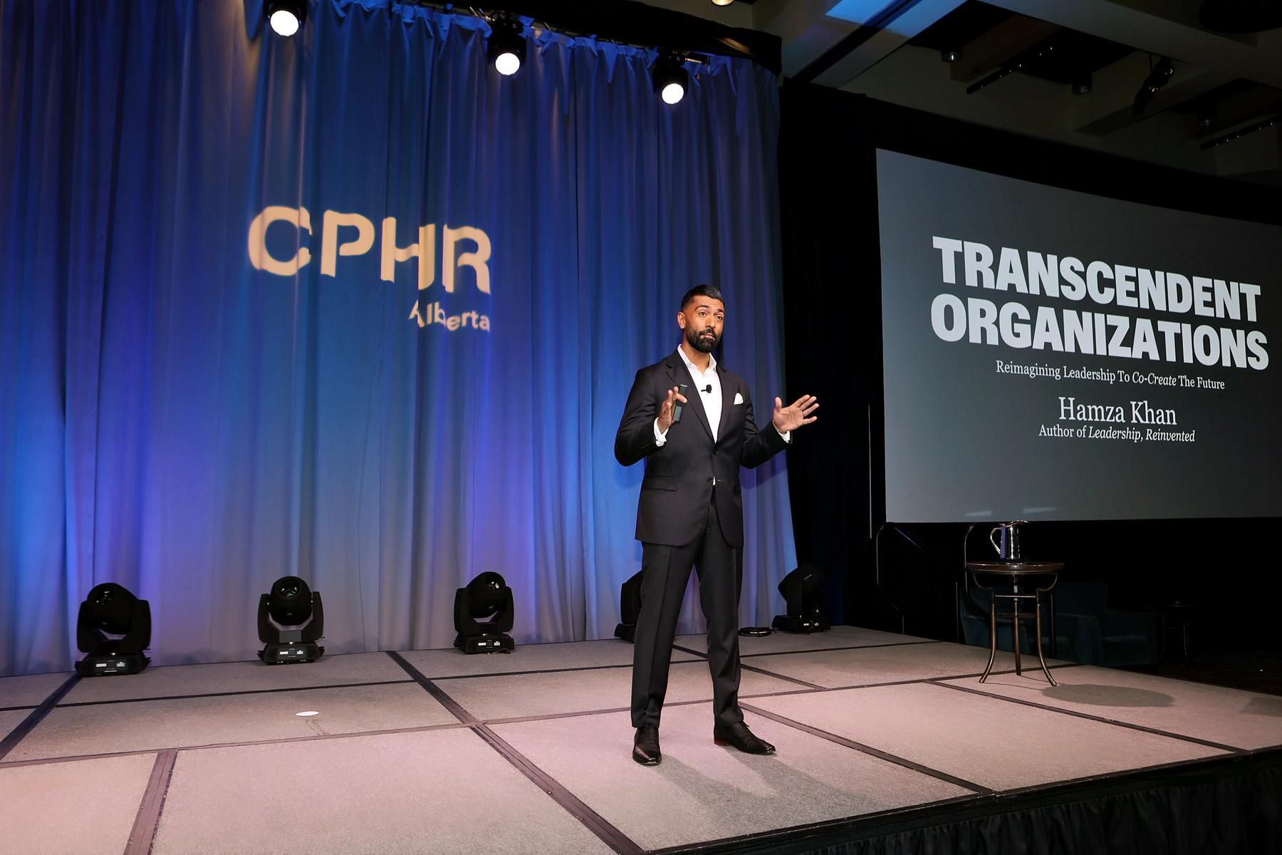 A man is standing on a stage in front of a screen that says transcendent organizations.