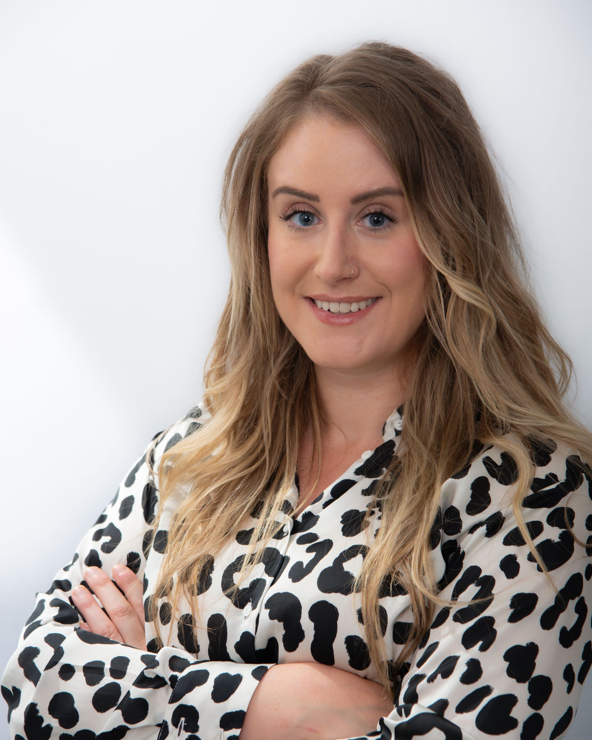 A woman in a leopard print shirt is smiling with her arms crossed.