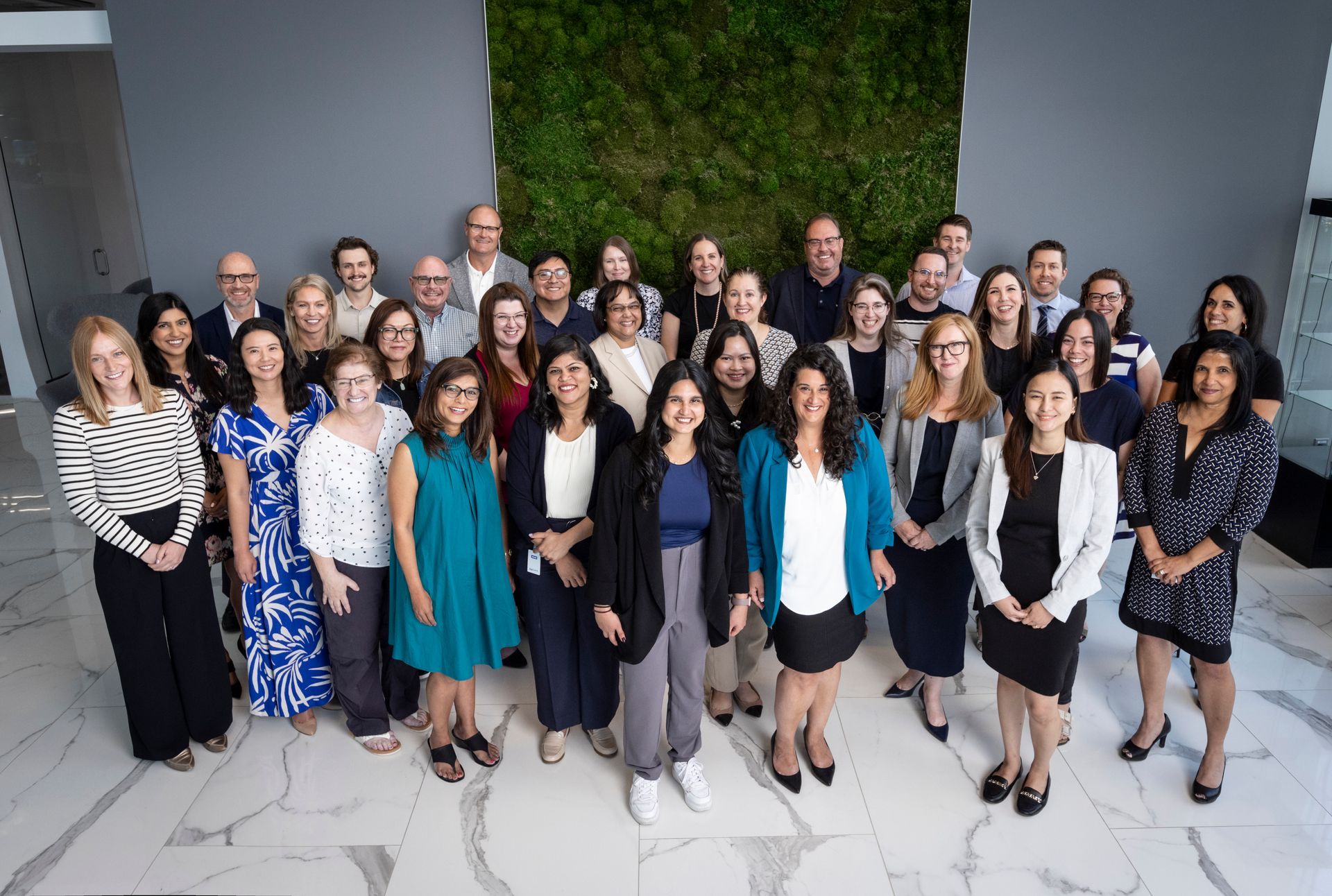 A large group of people are posing for a picture in front of a moss wall.