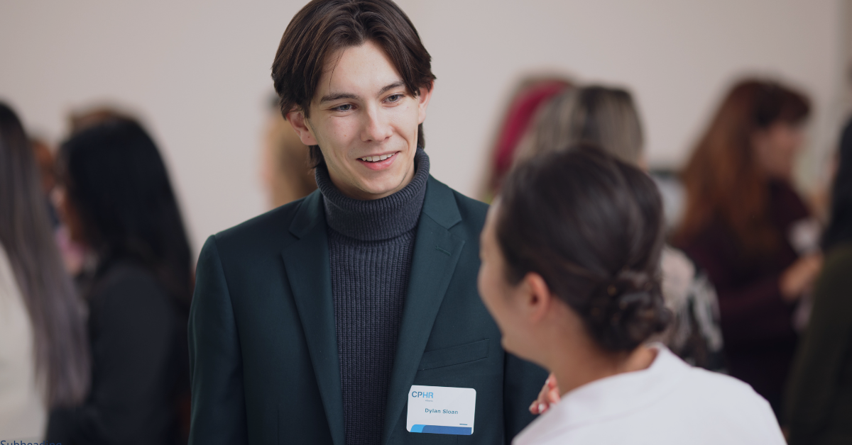 A man in a suit is talking to a woman in a crowd of people.