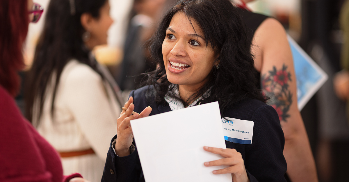 A woman is holding a piece of paper and smiling at a job fair.