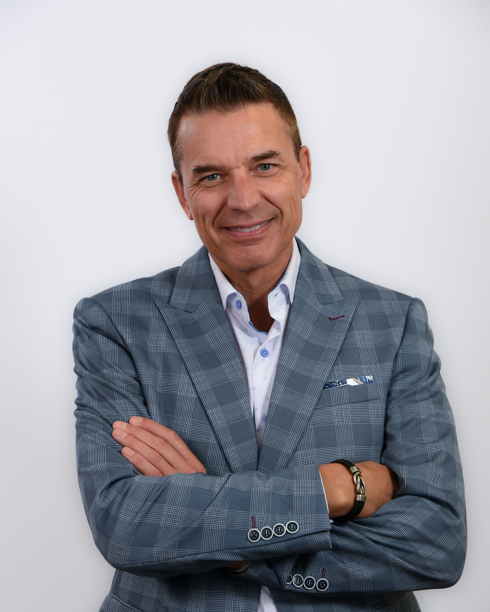 A man in a suit is standing with his arms crossed and smiling.