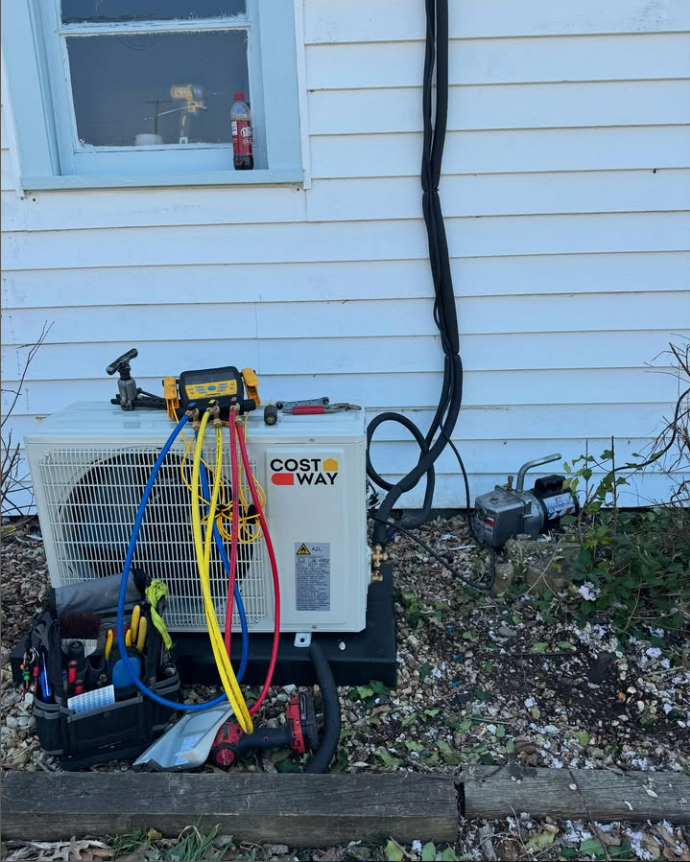HVAC technician servicing an air conditioner unit outside a light blue house.