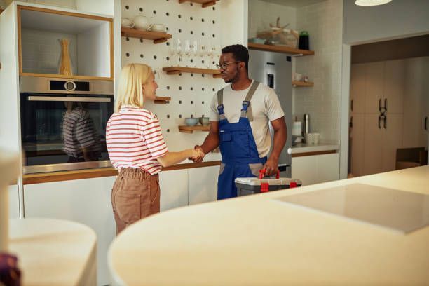 Woman shaking hands with a repairman in a kitchen. The man holds a toolbox.